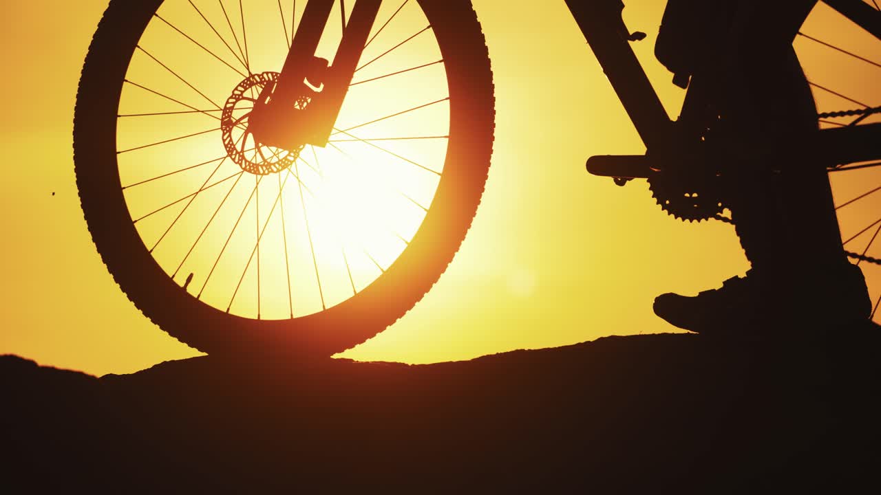 Amazing sunset and a big wheel of a bike in the evening. Silhouette of a bicycle on the background of golden sunset outdoors. Natural evening landscape and a bike. Close-up.