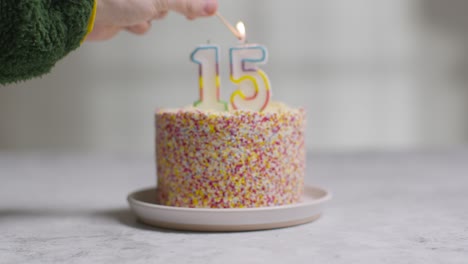 studio shot birthday cake covered with decorations and candle celebrating fifteenth birthday being lit