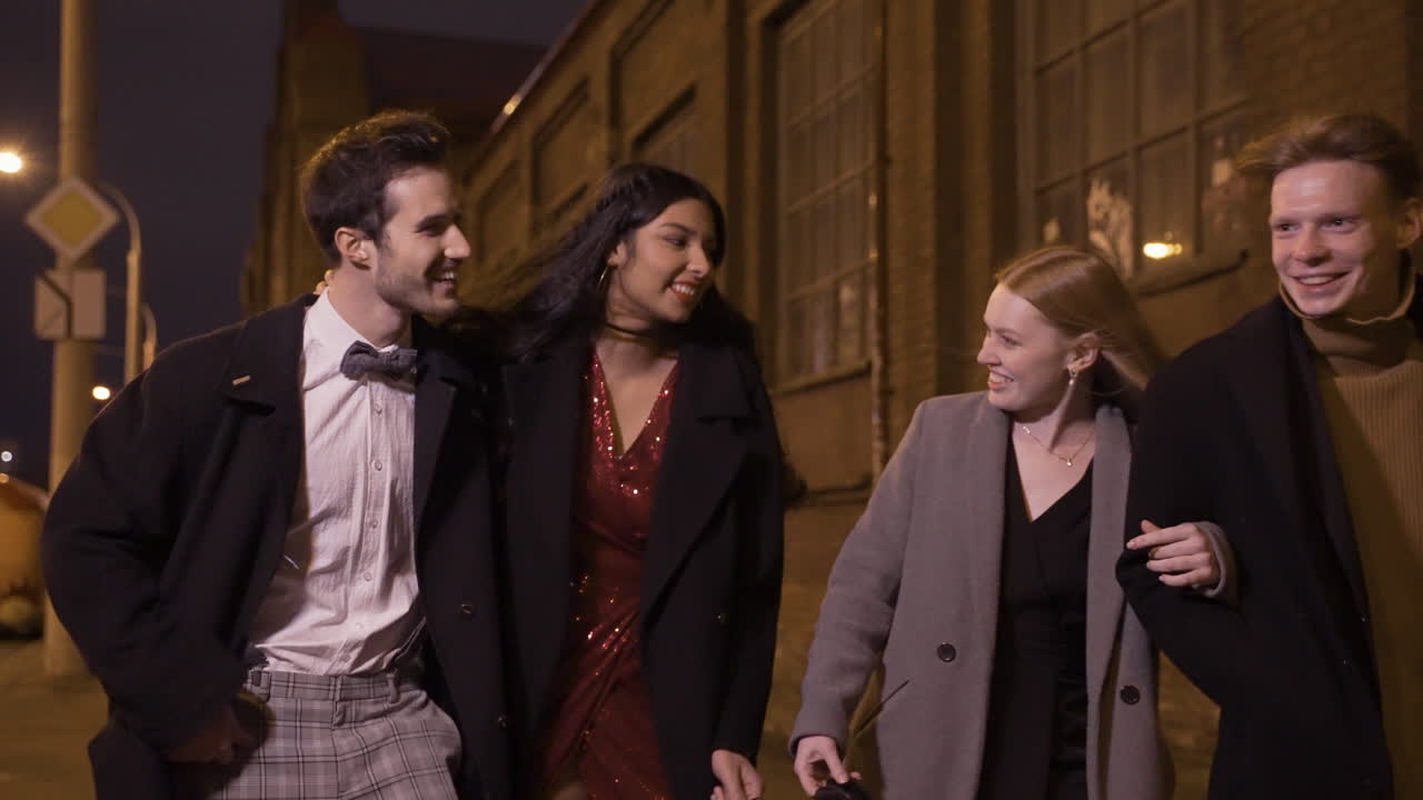 우아한 옷을 입은 두 커플의 친구가 신년 파티 후 이야기하고 웃으면서 거리를 걷고 있다