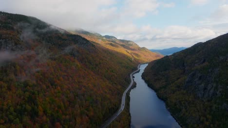 aerial view of a lake surrounded with fall foliage as cars passing by on the road in upstate new york