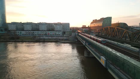 Vídeo-De-Drones-Del-Tranvía-De-Viena-Cruzando-El-Puente-Sobre-El-Río-Durante-La-Puesta-De-Sol-Dorada