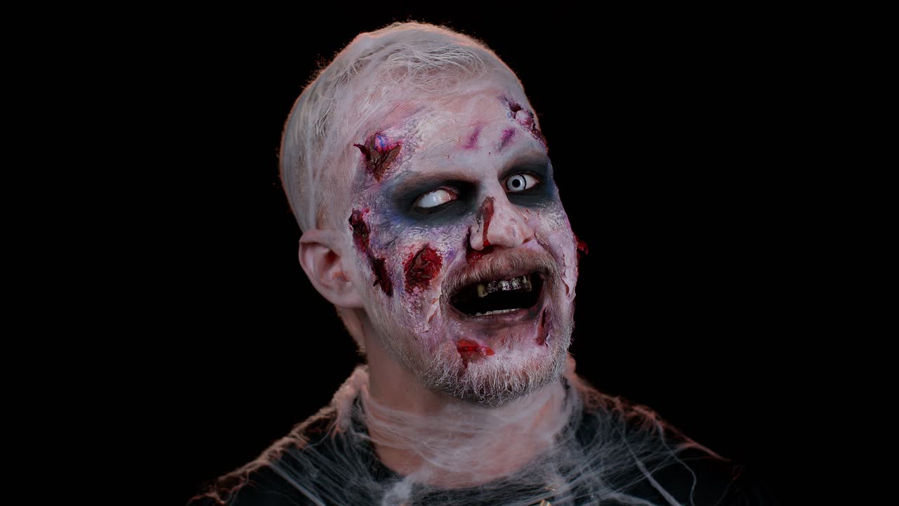 Zombie man with makeup with fake wounds scars and white contact lenses looking at camera, screaming
