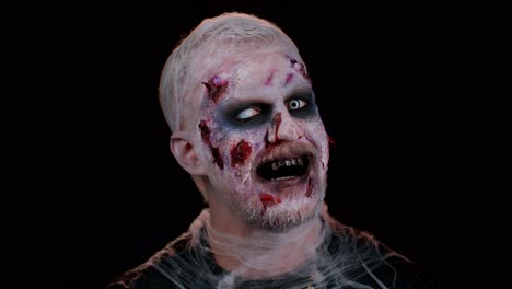 zombie man with makeup with fake wounds scars and white contact lenses looking at camera, screaming