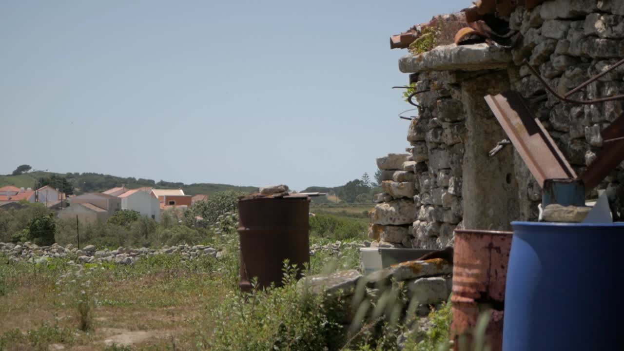 들판에 버려진 녹슨 드럼 컨테이너가 있는 오래된 석조 주택의 전망