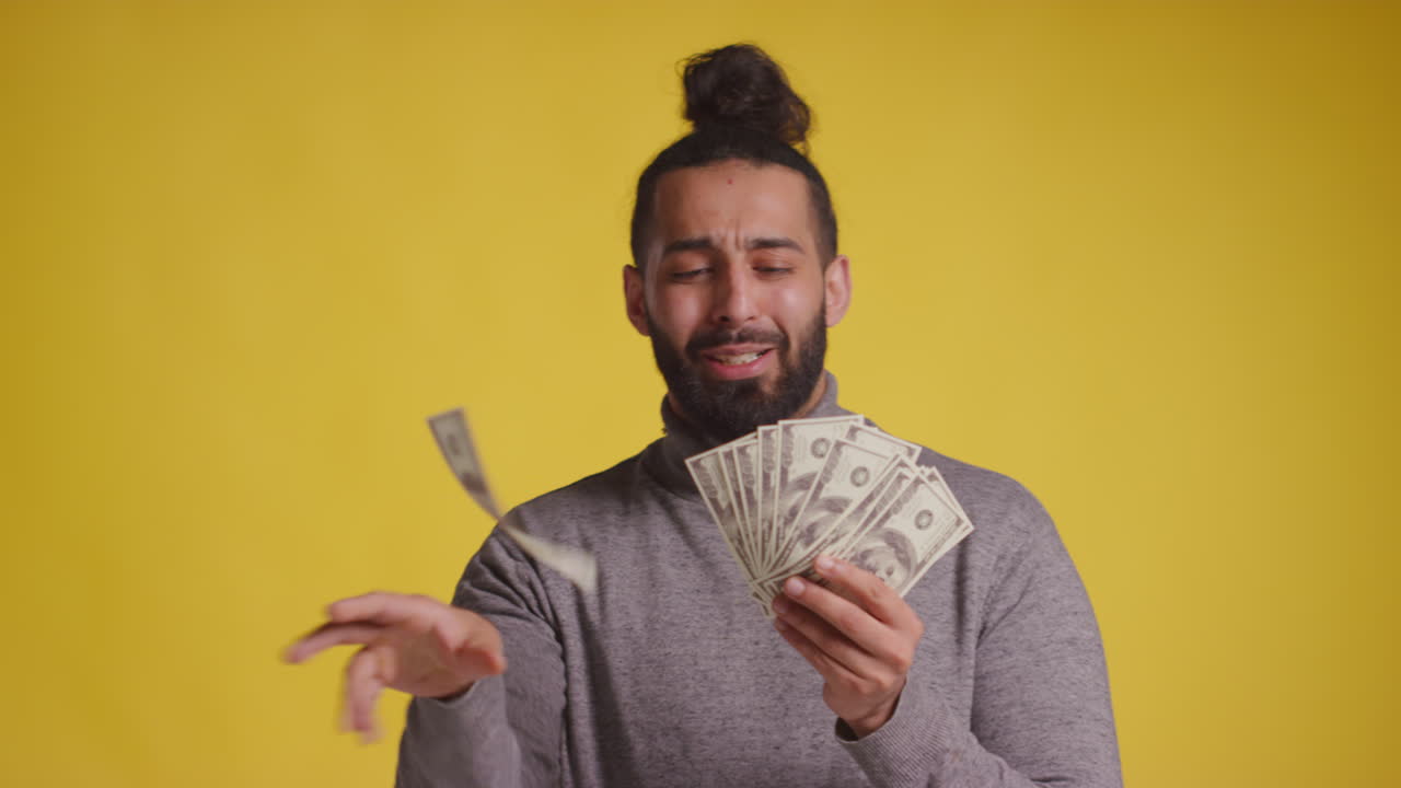 fotografía de estudio de un joven emocionado celebrando la ganancia de un premio en efectivo lanzando un puñado de billetes de 100 dólares en el aire contra un fondo amarillo