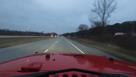 POV-while-driving-red-vehicle-down-an-interstate-at-dusk-on-a-rainy,-cloudy-day