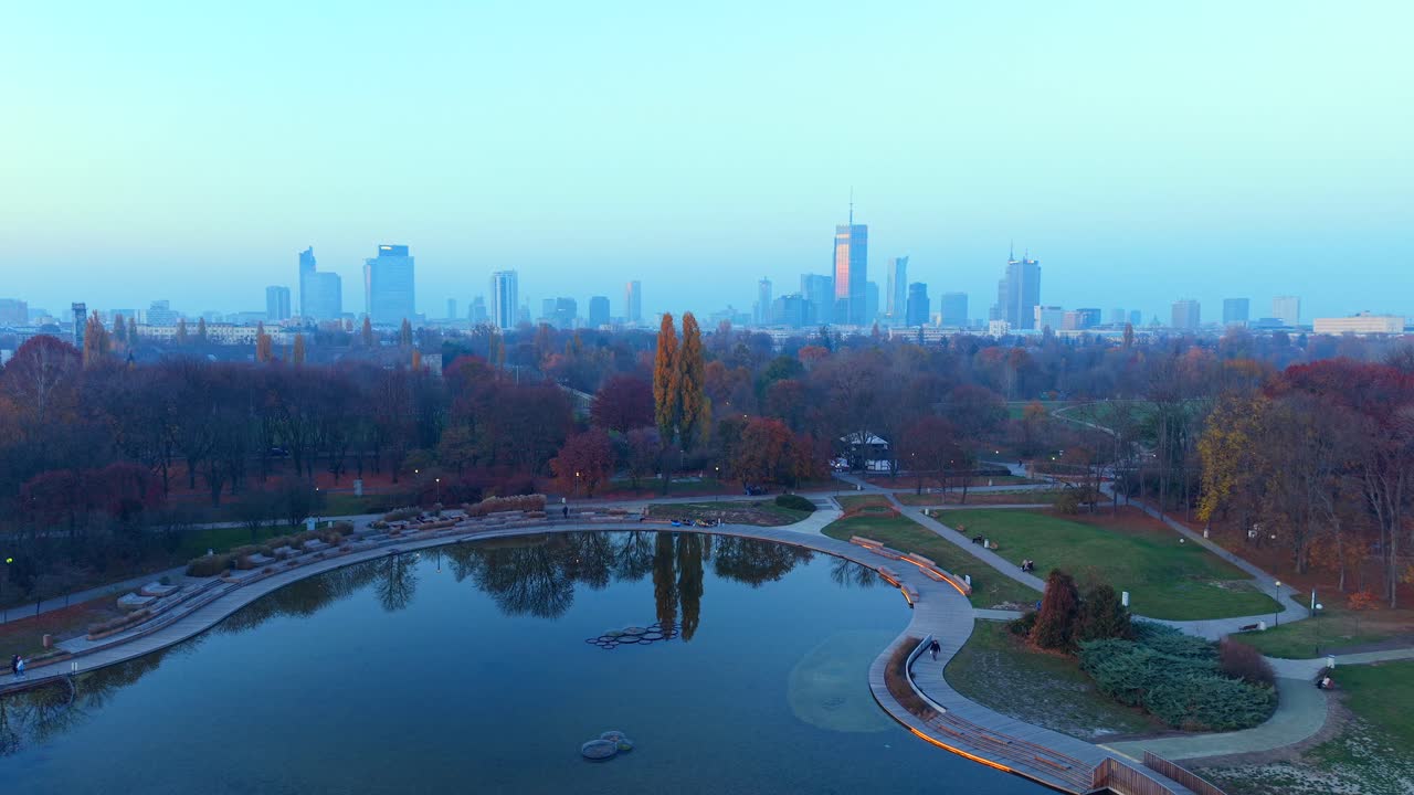 Warsaw, Poland. Aerial View of Park Lake and Misty Cityscape Skyline on Autumn Sunset, Drone Shot