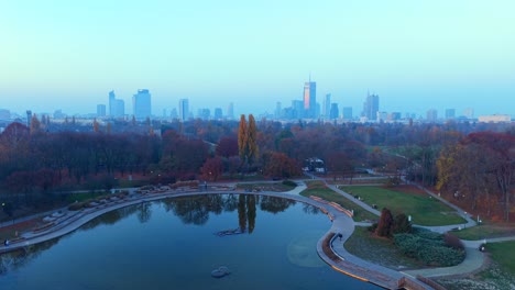 warsaw, poland. aerial view of park lake and misty cityscape skyline on autumn sunset, drone shot