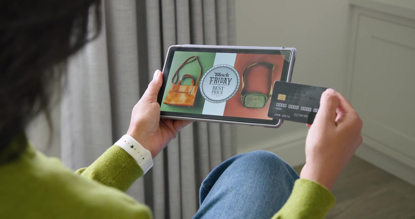 Adult woman sitting at home viewing Black Friday badge on tablet while aligning card and paying