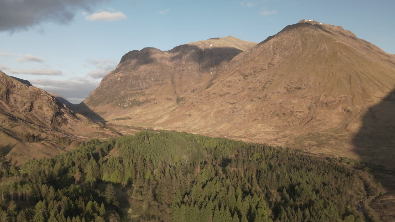 Drone flying through valley, featuring forrest below and mountains in the background