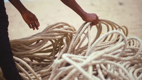 hands of unidentifiable fisherman collecting thick rope at shore