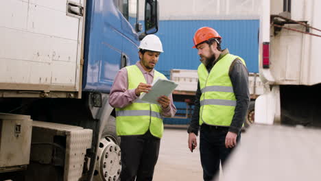 boss and worker wearing vests and safety helmets organizing a truck fleet in a logistics park while they consulting a document 5