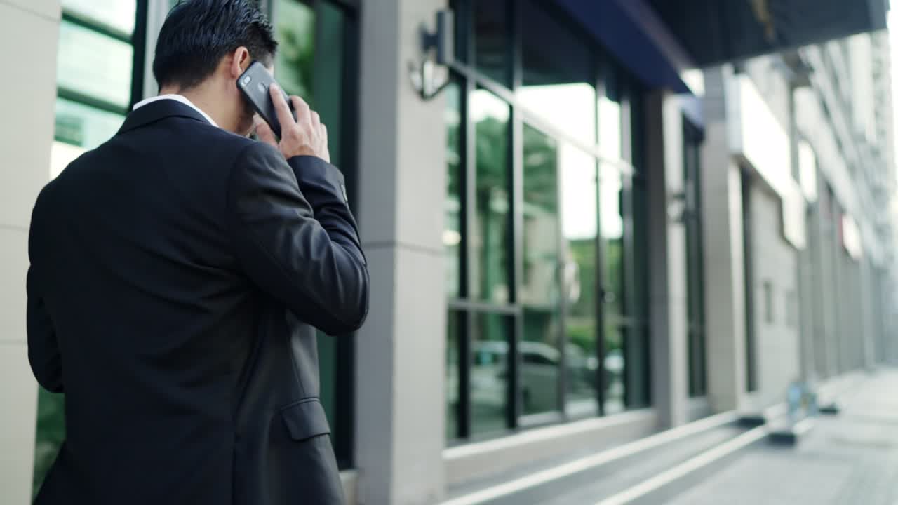 검은색 슈트를 입은 아시아 사업가가 도시의 거리를 고 있습니다. 작업에 가십시오. 스마트폰을 사용하여 손에 들고. 도시 라이프 스타일 컨셉.