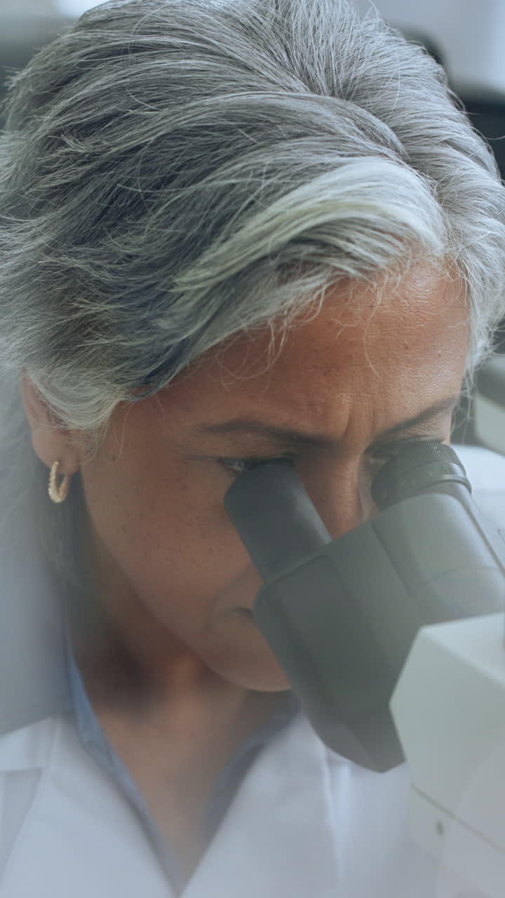 Scienziata matura che guarda attraverso un microscopio in un laboratorio