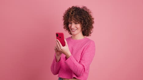cheerful woman taking selfie with smartphone in pink studio