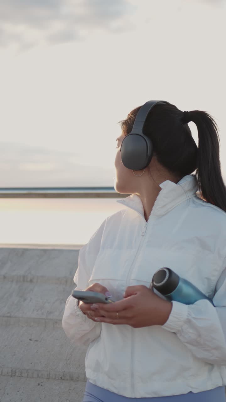 Giovane donna con cuffie e smartphone che si riposa all'aperto.