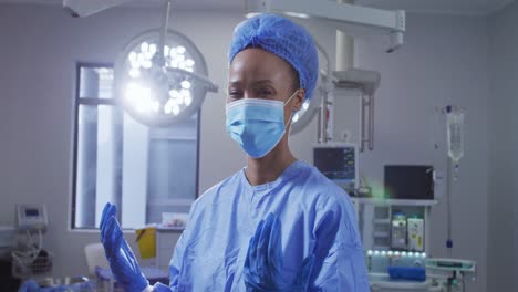 Portrait-of-mixed-race-female-surgeon-wearing-face-mask-standing-in-operating-theatre