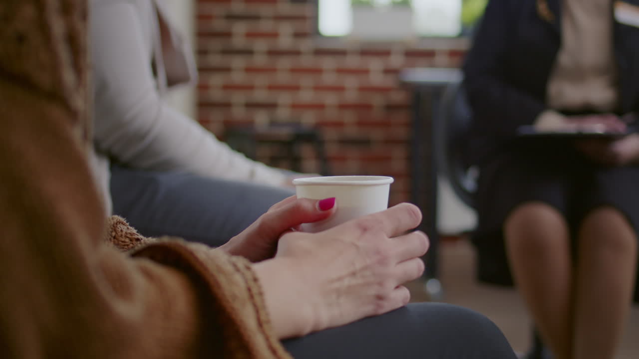 Close up of shaky woman feeling nervous while holding cup of coffee at aa group meeting