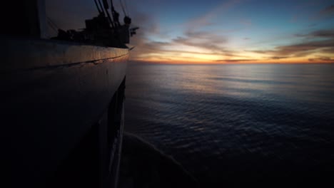 view-the-side-of-a-boat-when-it's-cruising-through-a-galssy-water-surface-in-the-sunset