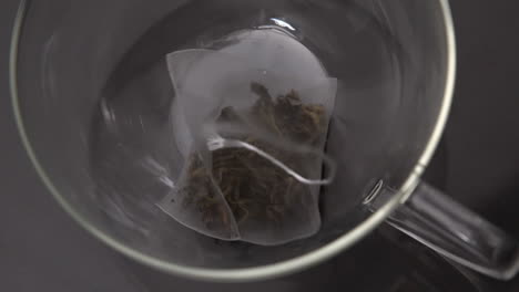 una bolsa de té cayendo en una taza de vidrio