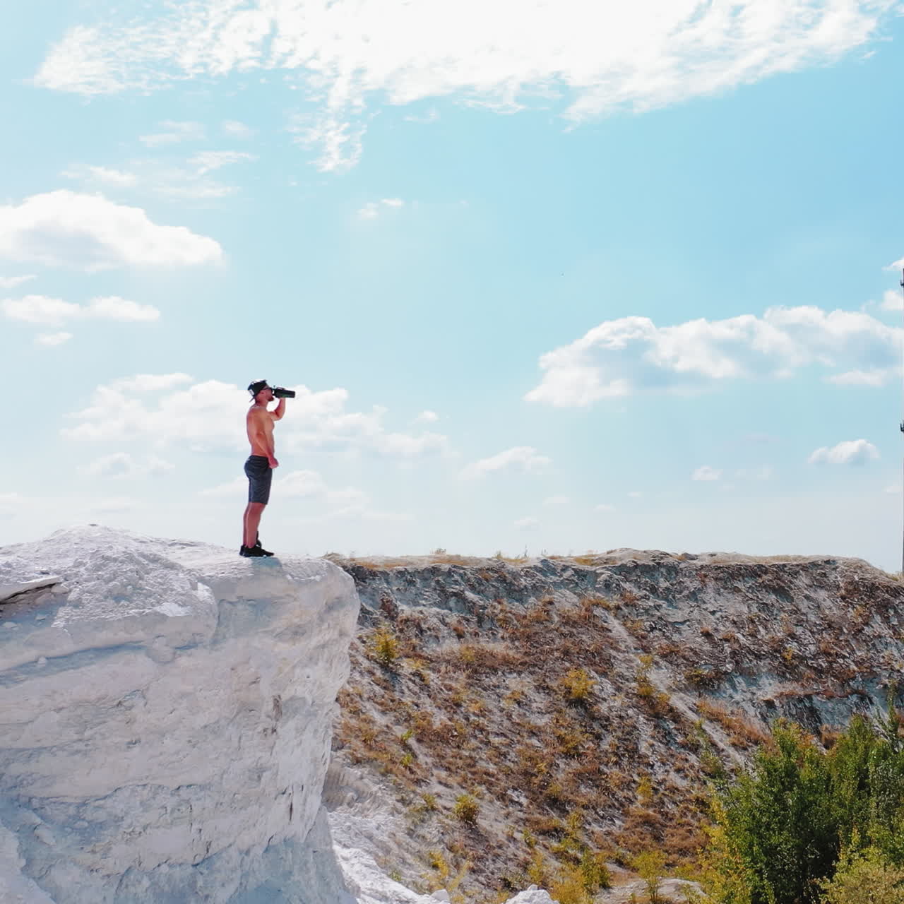 Brutal strong bodybuilder posing outdoor. Photoshoot in a quarry. Outdoor sports concept. Aerial view. Handsome strong man drinks water outdoor. White landscape.