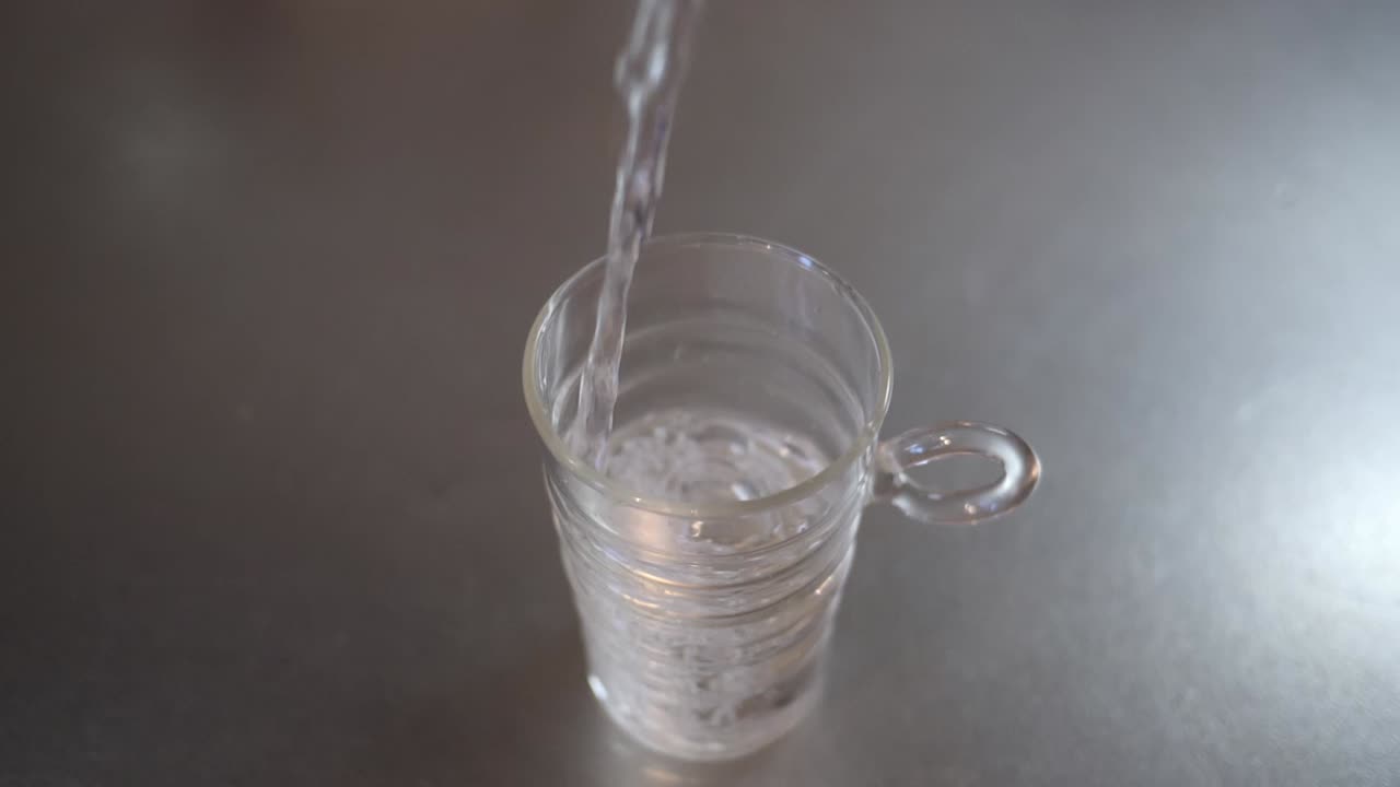 금속 주방 작업대에 있는 유리컵에 물을 붓는 각도 전체 샷, 건강과 깨끗한 물 개념, 슬로우 모션 영상