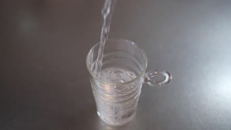 금속 주방 작업대에 있는 유리컵에 물을 붓는 각도 전체 샷, 건강과 깨끗한 물 개념, 슬로우 모션 영상