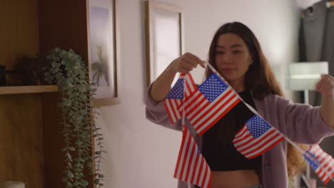 woman at home hanging up american stars and stripes flag bunting for party celebrating 4th july independence day 4