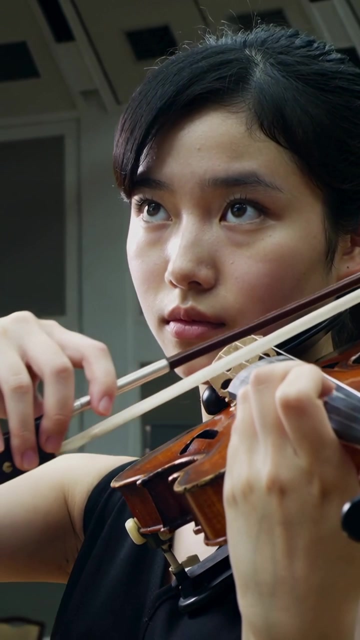 Vertical video: Starting violinist in black dress lifting gaze and drawing bow in rehearsal room