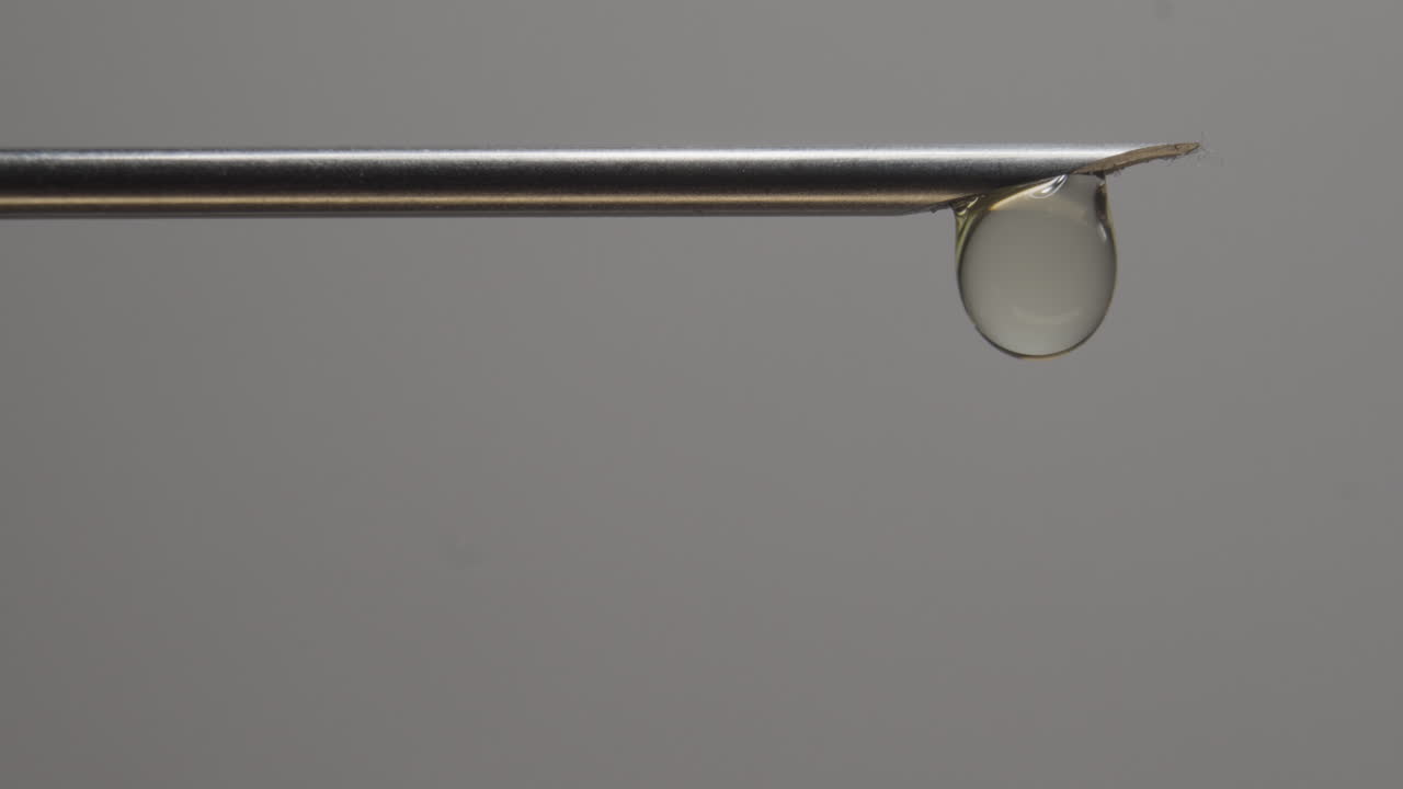 una sola gota de líquido que cae de la punta de la aguja hipodérmica en un primer plano extremo