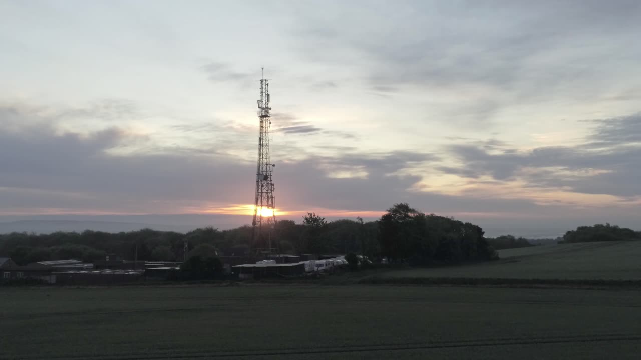 Sunrise lifting through telecom towers rising aerial view on agricultural farmland at dawn