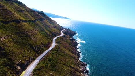 aerial drone shot of a road on the cliff side between the mountain and the sea