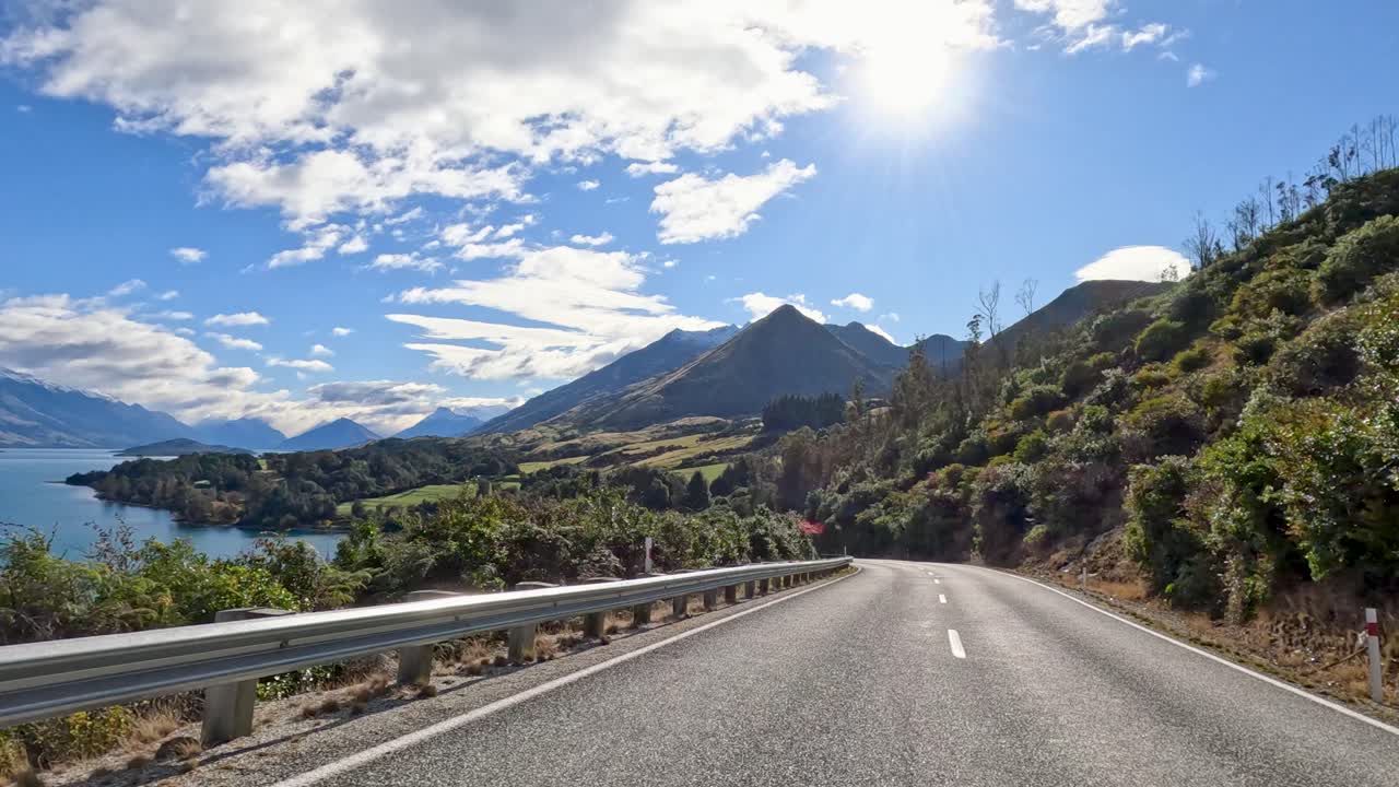 A 20-second drive along a winding road in Queenstown, New Zealand, showcasing stunning mountain and lake views under bright sunlight