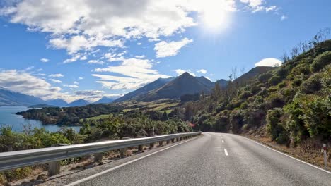 a 20-second drive along a winding road in queenstown, new zealand, showcasing stunning mountain and lake views under bright sunlight