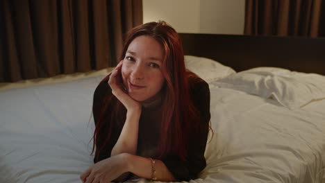 attractive young woman lies in bed and smiles towards camera