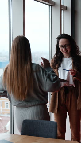 business people communicating about work. ladies discuss working issues standing at the window in office. vertical video