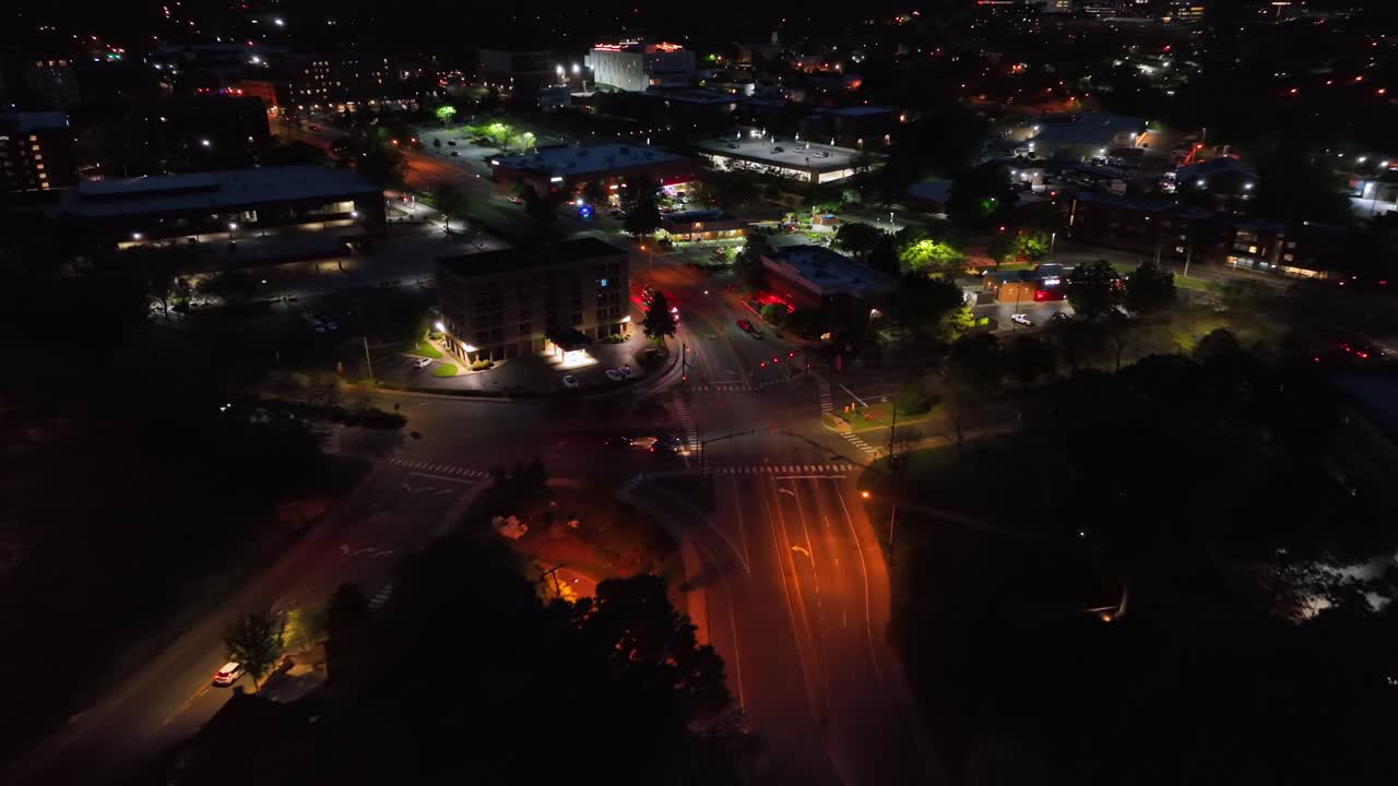 Fire truck turning on junction into illuminated street at night. Aerial approaching shot. Flashing red lights during emergency operation. Cityscape with gas station in distance. Charlottesville,VA.
