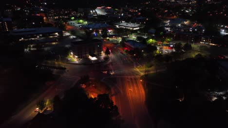 fire truck turning on junction into illuminated street at night. aerial approaching shot. flashing red lights during emergency operation. cityscape with gas station in distance. charlottesville,va.