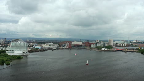 Aerial-Flyover-of-Cardiff-Bay-towards-the-Quayside-on-a-Cloudy-Summer’s-Day-with-Passenger-Ferry---Sailboat-in-Foreground