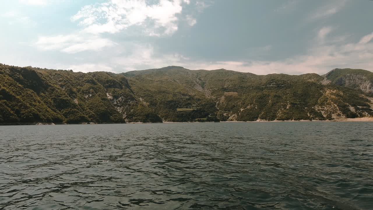 Peaceful mountain lake on high Alps with sharp slopes full of green vegetation under cloudy sky in Albania