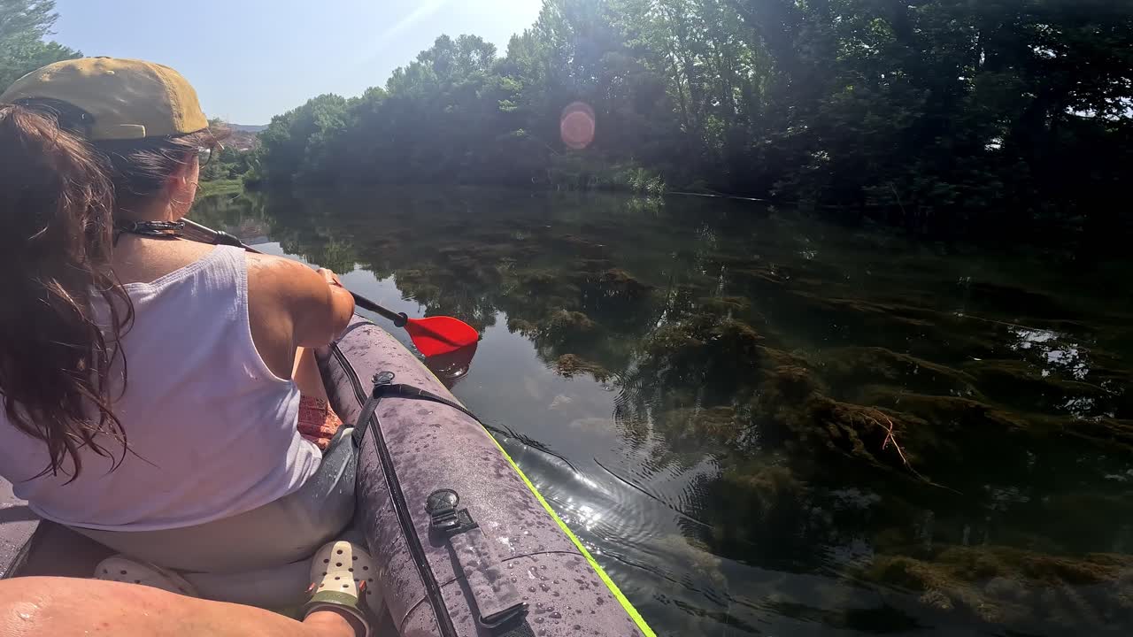 A woman leisurely paddling a kayak down a calm river, surrounded by lush trees and clear water reflecting the blue sky
