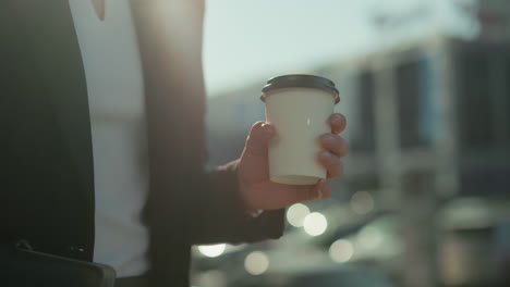 Close up of young girl in business outfit walking while holding tea cup under daylight, cityscape with bokeh lights, parked cars, and urban background