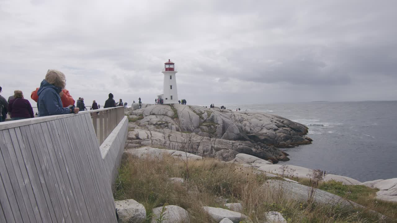 Tourists visiting Peggy's Cove Lighthouse on a cloudy day by the rocky coastline in Canada