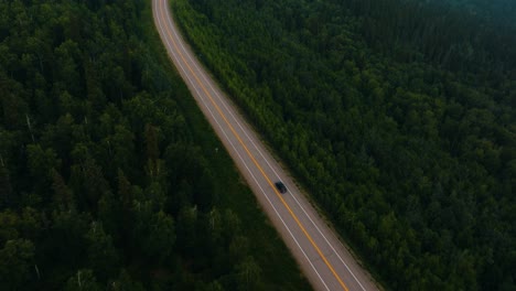 aerial drone follow of lone car driving on two lane tree lined highway in the middle of nowhere alaska