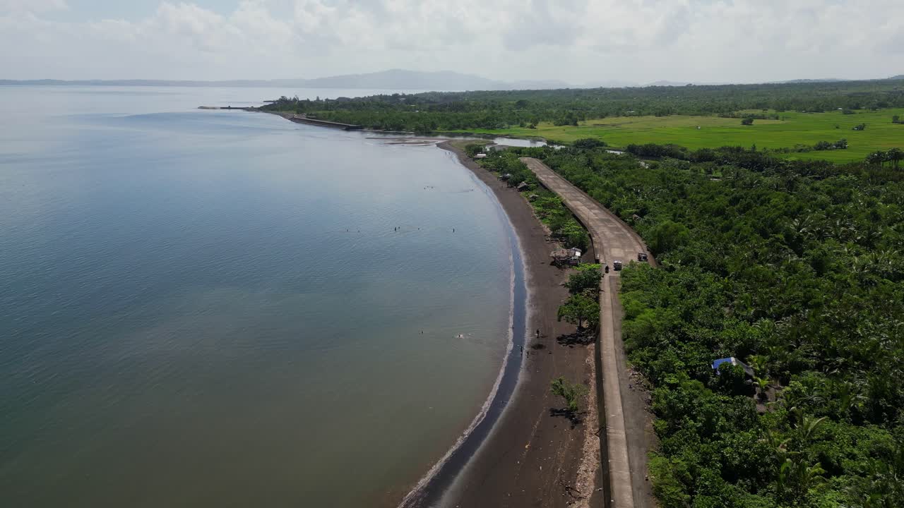 Lush Green Shoreline With Calm Waters And Rural Road In Malilipot, Albay, Philippines. aerial shot