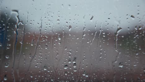 Rain-drops-on-clear-glass-window-cascading-down,-close-up-static-shallow-depth-of-focus