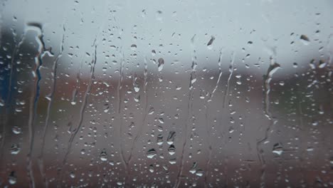 rain drops on clear glass window cascading down, close up static shallow depth of focus