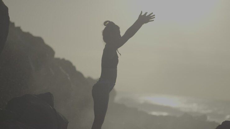 Mulher praticando yoga em uma praia rochosa ao nascer ou pôr do sol