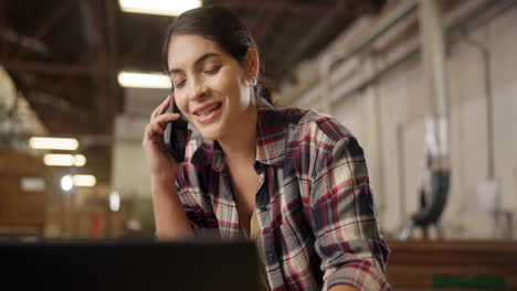 woman talking on phone while working on laptop in workshop