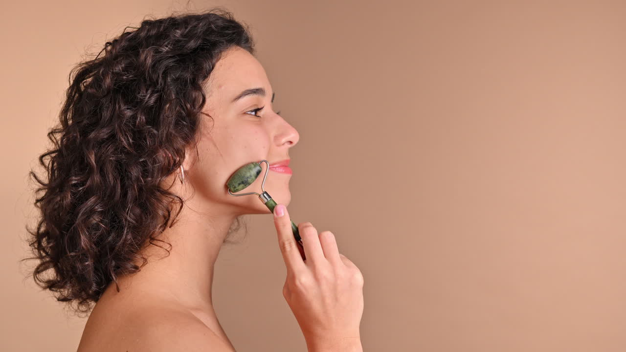 A young caucasian smiling woman is doing a facial massage using a roller